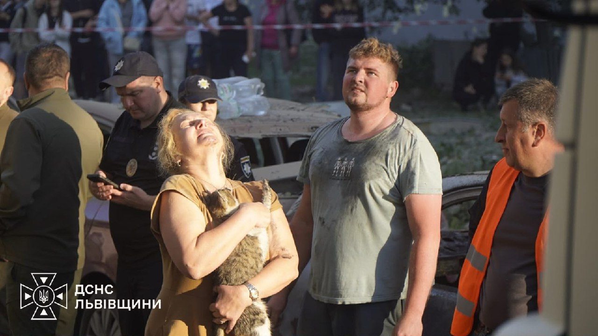Мешканці біля зруйнованої ракетним ударом багатоповерхівки у Львові — жінка з врятованим котом, поруч поліція і рятувальні служби